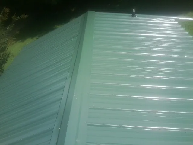 New green metal panels meeting at the ridge of a roof — Flat Roof Repair work by our crew in Berea