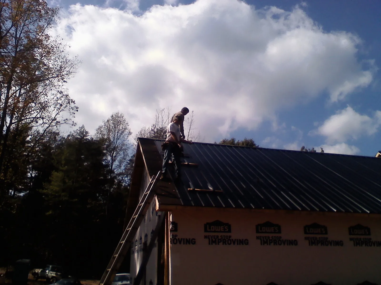 Roofer fastening dark metal panels high against a cloudy sky, from a Roof Inspection job in Berea